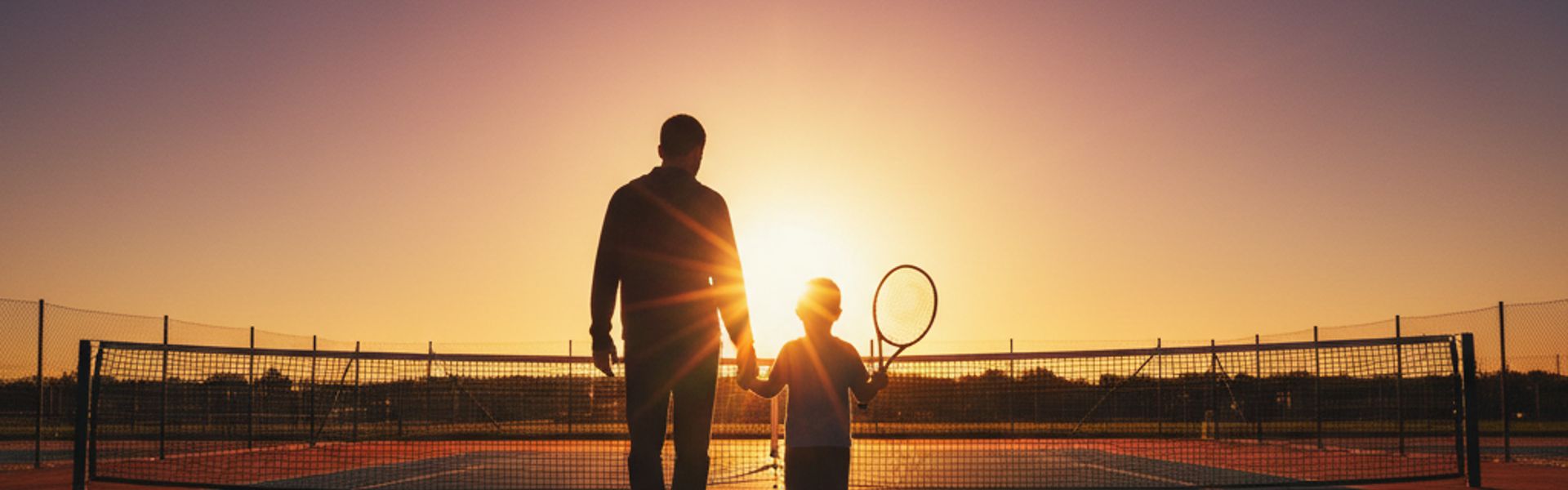 Parent and child walking onto tennis court at sunset
